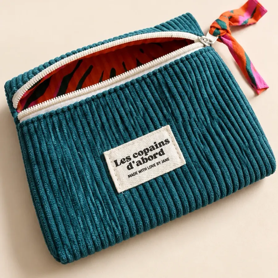 Pochette en velours côtelé bleu canard entrouverte sur sa doublure zébrée orange et rose, tirette nouée assortie, étiquette Les copains d’abord