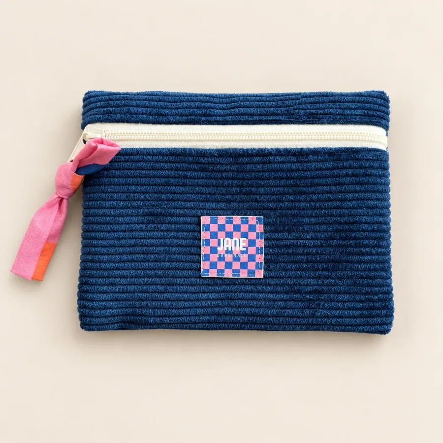 Pochette plate en velours côtelé bleu marine, fermeture écrue, tirette nouée rose et orange, étiquette Jane à damier rose et bleu