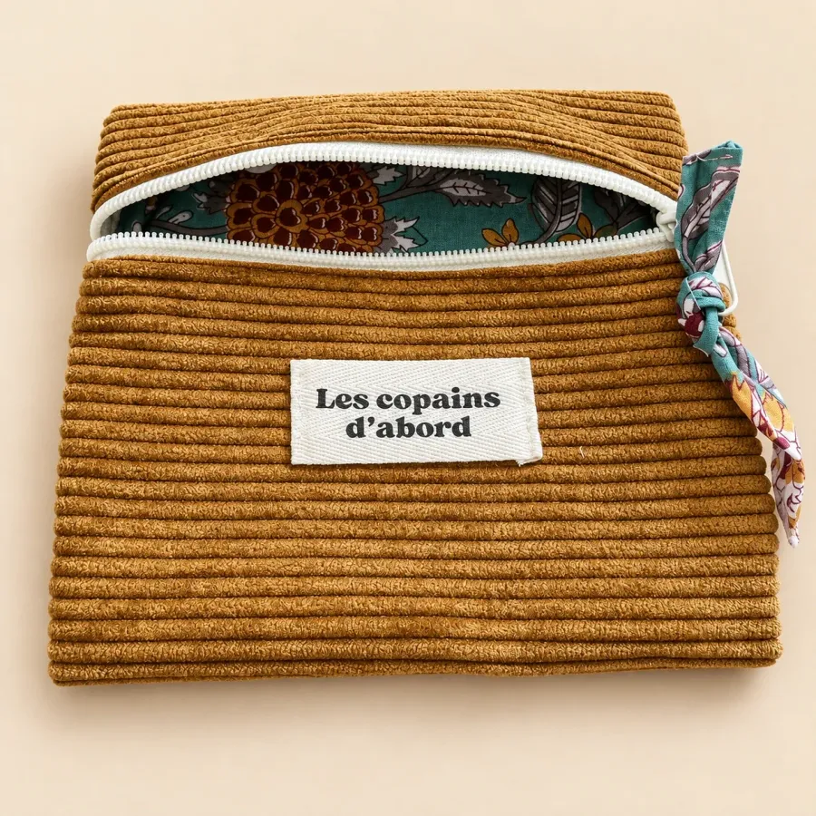 Pochette ocre entrouverte sur sa doublure fleurie turquoise, étiquette Les copains d’abord