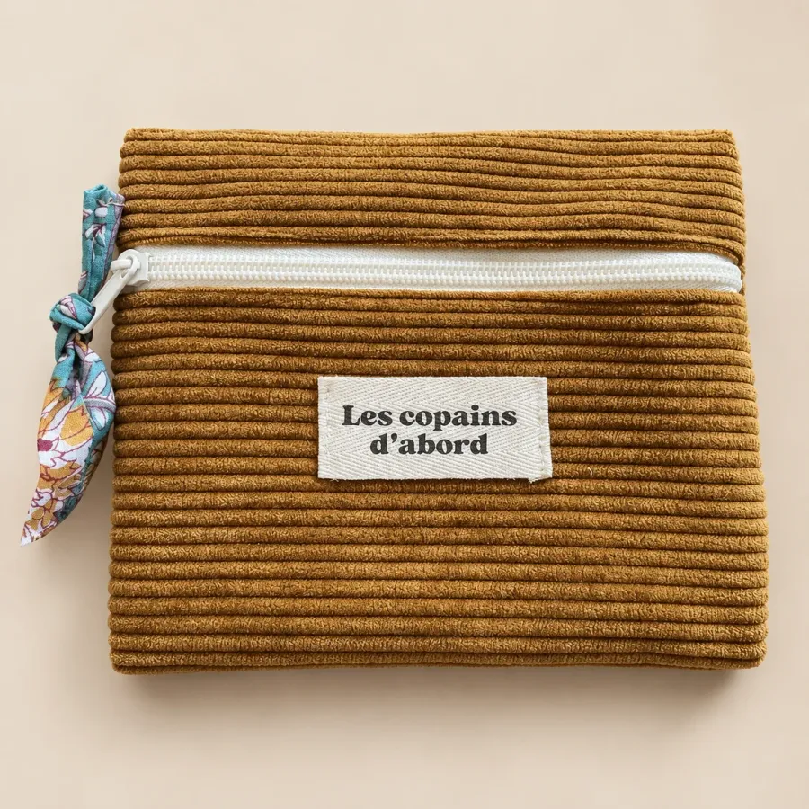 Pochette plate en velours côtelé ocre, fermeture écrue, tirette nouée en tissu fleuri, étiquette Les copains d’abord