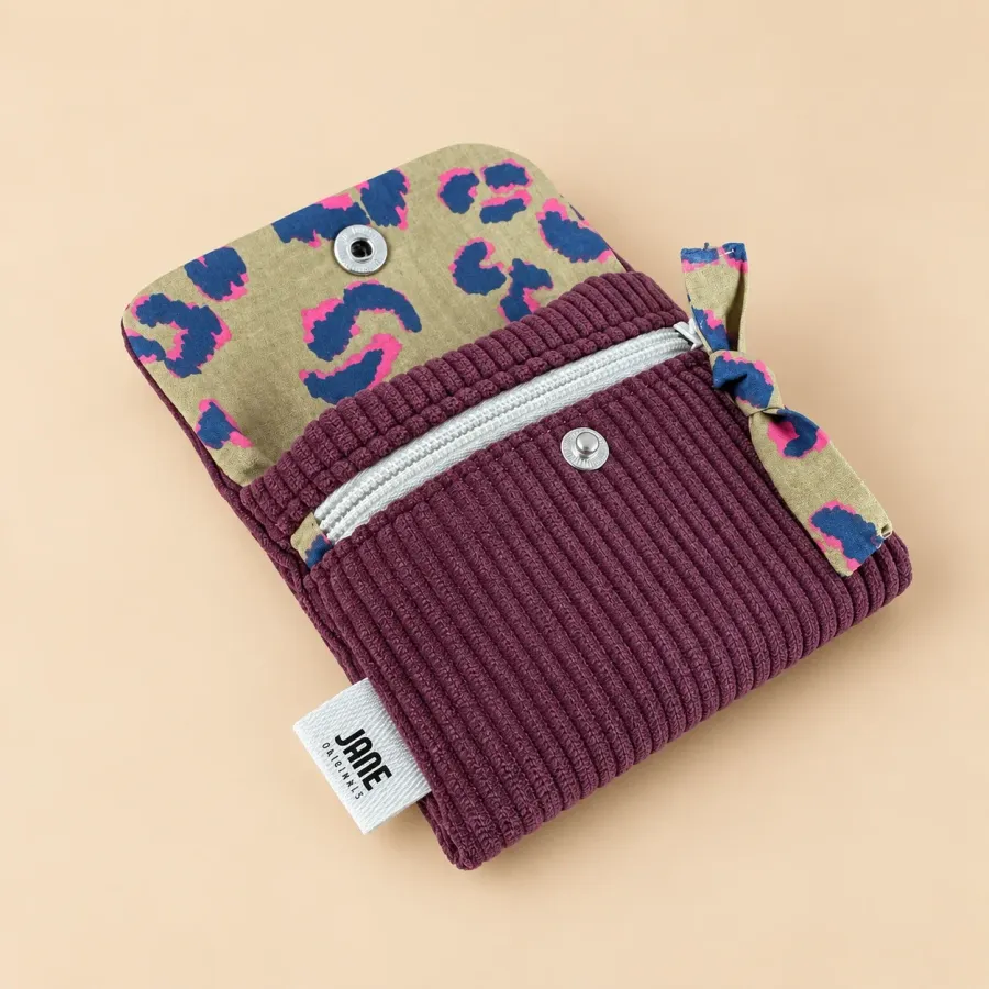 Porte-cartes bordeaux ouvert, rabat doublé d’un tissu léopard bleu et rose sur fond kaki, poche zippée blanche