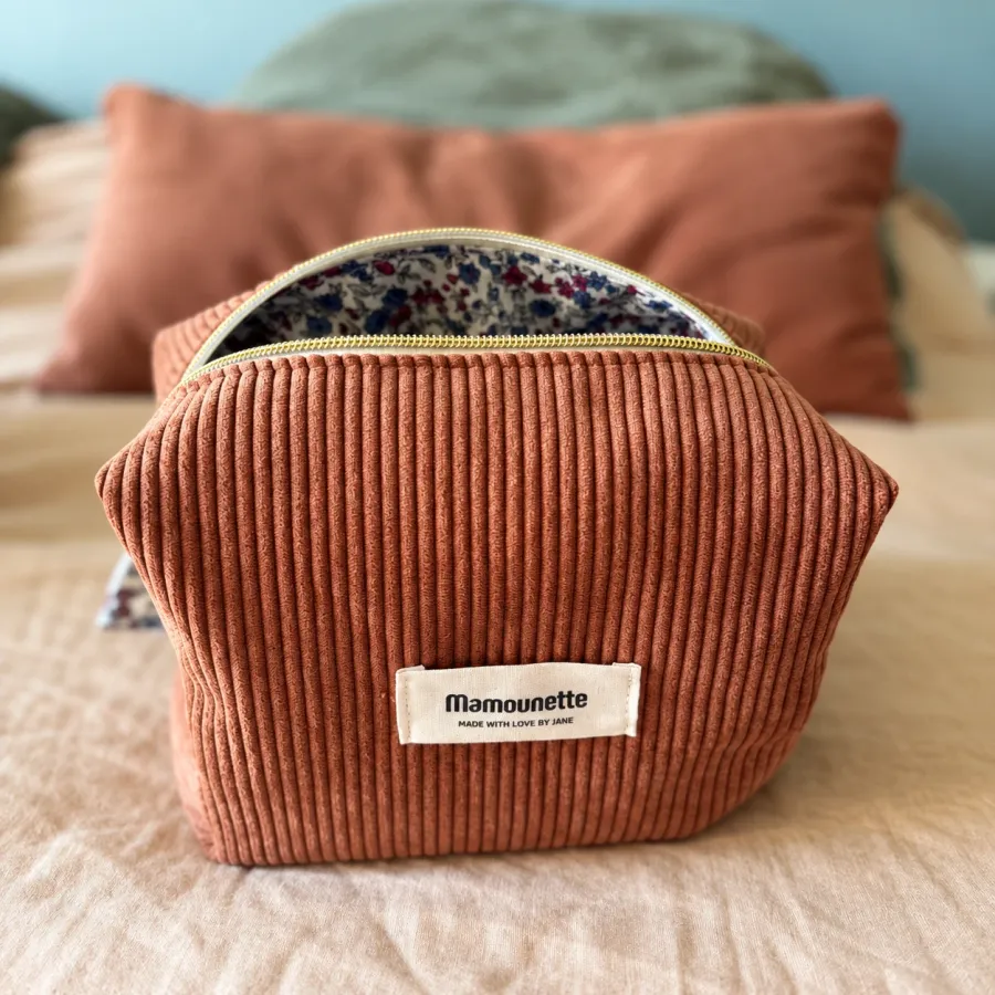 Trousse terracotta ouverte sur sa doublure fleurie, posée sur un lit